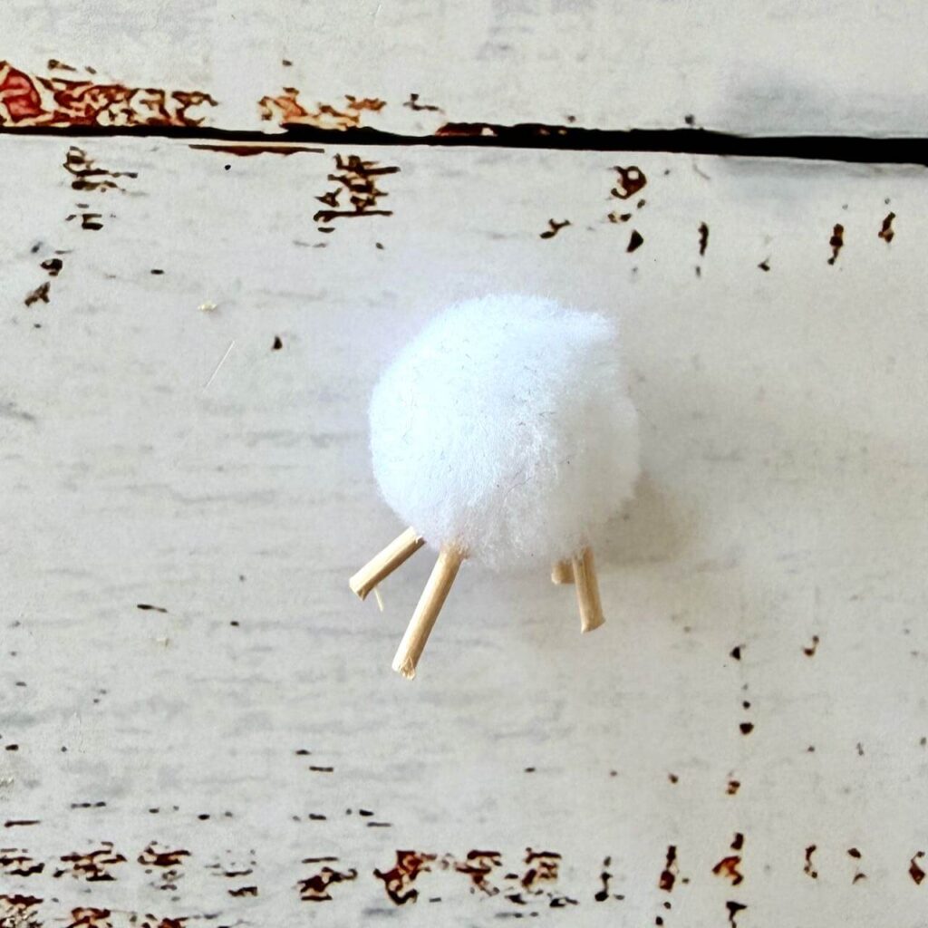 Weißer Pompon mit vier Füßen aus Schaschlikspießen für den Schafkörper