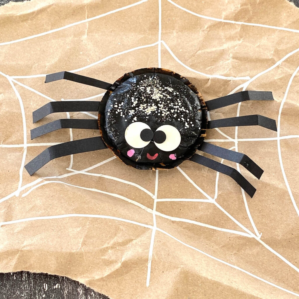 Geniale Halloween Deko basteln: 5 nachhaltige & einfache Ideen 8 Gebastelte Spinne aus einem Kaffeepad und Papierbeinen auf einem gezeichneten Spinnennetz aus Packpapier.